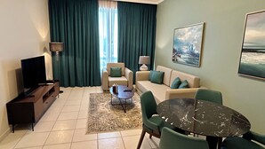 Una sala de estar con sofá, sillas, televisor, mesa y un ventanal con cortinas.