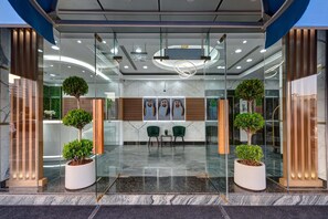 A modern reception area with glass walls, two potted plants, a seating area with chairs, and a marble floor.