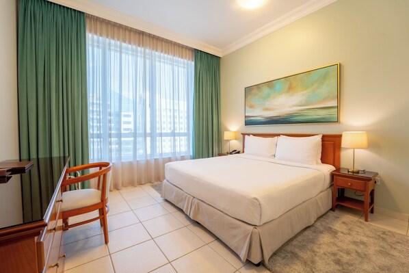 A hotel room with a bed, a desk, a chair, a painting on the wall, and two bedside lamps.