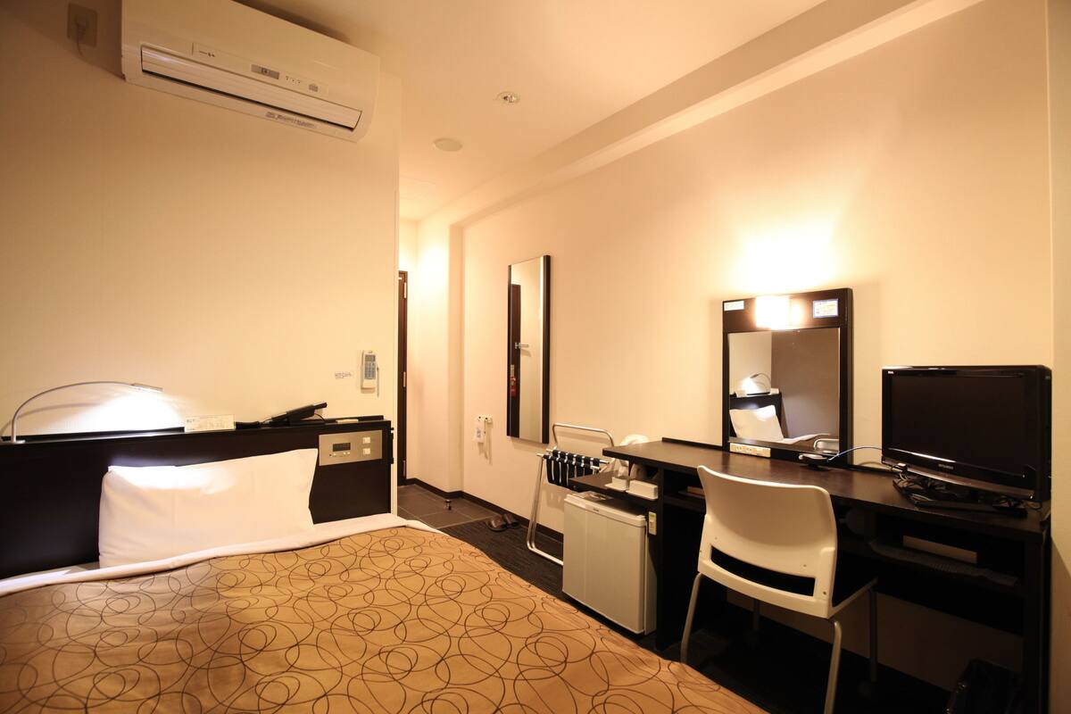 A hotel room with a bed, desk, chair, and a television.