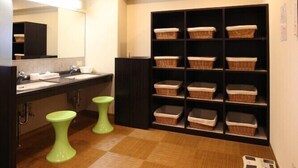 A bathroom with a vanity, two green stools, a shelf with baskets, a scale, and a wall-mounted fan. - Az Inn Higashiomi Notogawa Ekimae (Higashiomi)