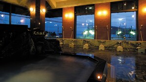 A hot spring bath area with stone seating and a view of the cityscape through large windows. - Kinpokan (Toba)