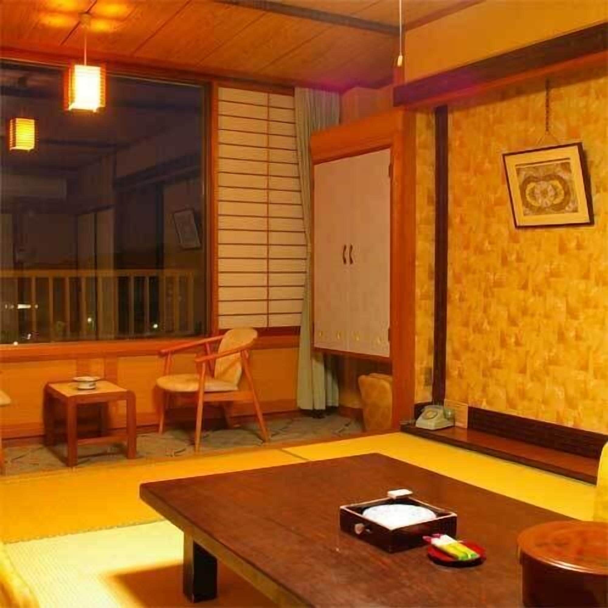 A room with tatami flooring, a low table with a tray, a chair, a cabinet, and a window with blinds.