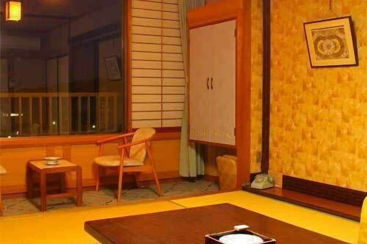 Una habitación con suelo de tatami, una mesa baja con una bandeja, una silla, un armario y una ventana con persianas.
