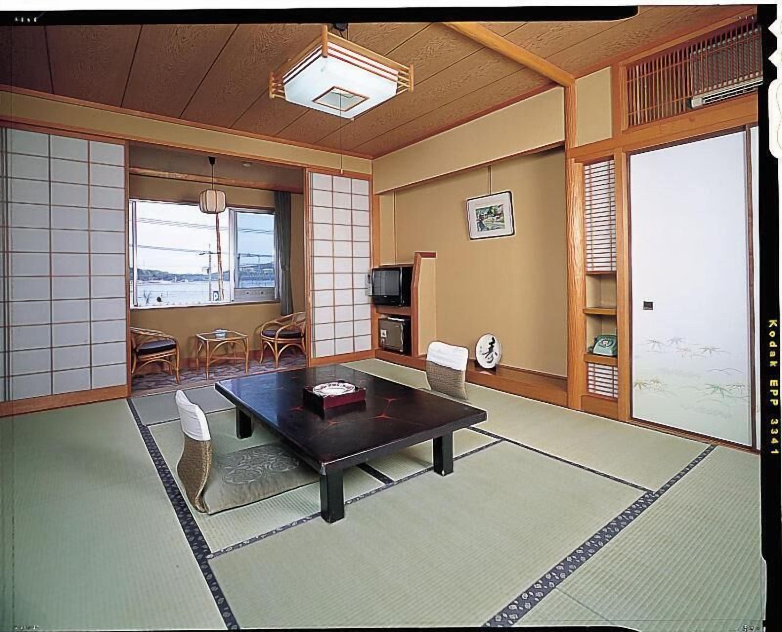 A traditional Japanese room with tatami flooring, a low table, chairs, a television, and a sliding door.