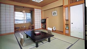 A traditional Japanese room with tatami flooring, a low table, chairs, a television, and a sliding door.