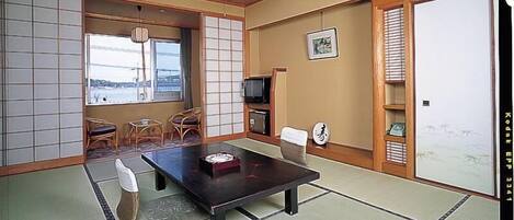 A traditional Japanese room with tatami flooring, a low table, chairs, a television, and a sliding door.