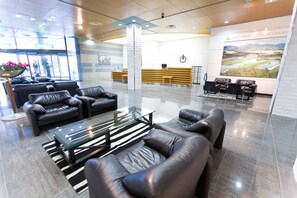 A modern lobby with leather sofas, a glass coffee table, and a reception desk.