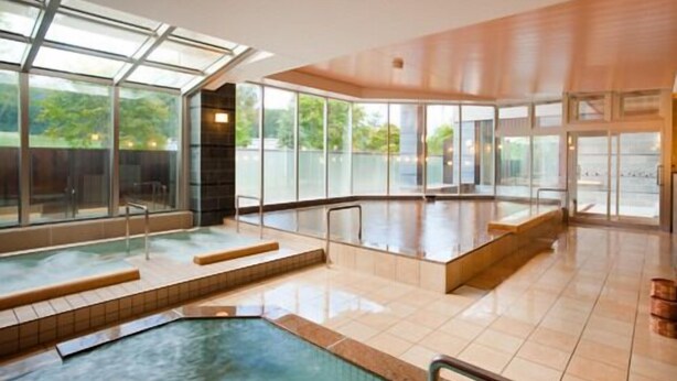 Une grande piscine intérieure aux parois en verre transparent, dotée d’un sol carrelé et d’un plafond en bois.