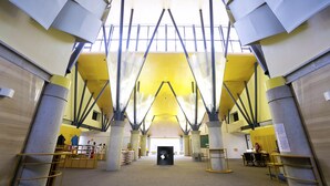 Un intérieur spacieux avec de hauts plafonds et des poutres apparentes, comprenant un espace central ouvert et plusieurs coins salon.