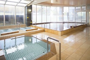 A large indoor swimming pool with clear glass walls, tiled floors, and a wooden deck area.