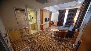 Habitación de hotel con alfombra estampada, sofá, una mesita redonda, televisor y zona de ducha.
