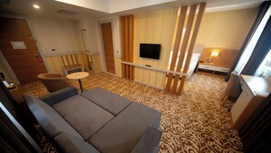 Habitación de hotel con sofá, una pequeña mesa redonda, televisor montado en la pared y alfombra estampada.