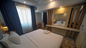 Habitación de hotel con una cama grande, un escritorio, una silla, un espejo y una alfombra estampada.