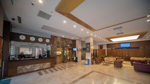 Un hall de hotel con mostrador de recepción, zona de estar y una pantalla de televisión.