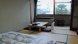 Um quarto japonês tradicional com tatames, um futon, uma mesa baixa com um conjunto de chá e vista para o exterior através de uma grande janela.
