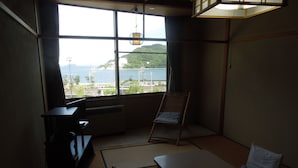 Quarto com piso de tatame, uma mesa baixa, uma cadeira e vista para o mar por grandes janelas.