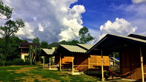 A row of simple, single-story cabins with open sides, surrounded by lush greenery and a clear sky. - Sleepy Hut Pai (Pai)