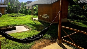 A hammock hanging under a wooden structure with a metal roof, surrounded by a grassy yard and a small pond. - Sleepy Hut Pai (Pai)
