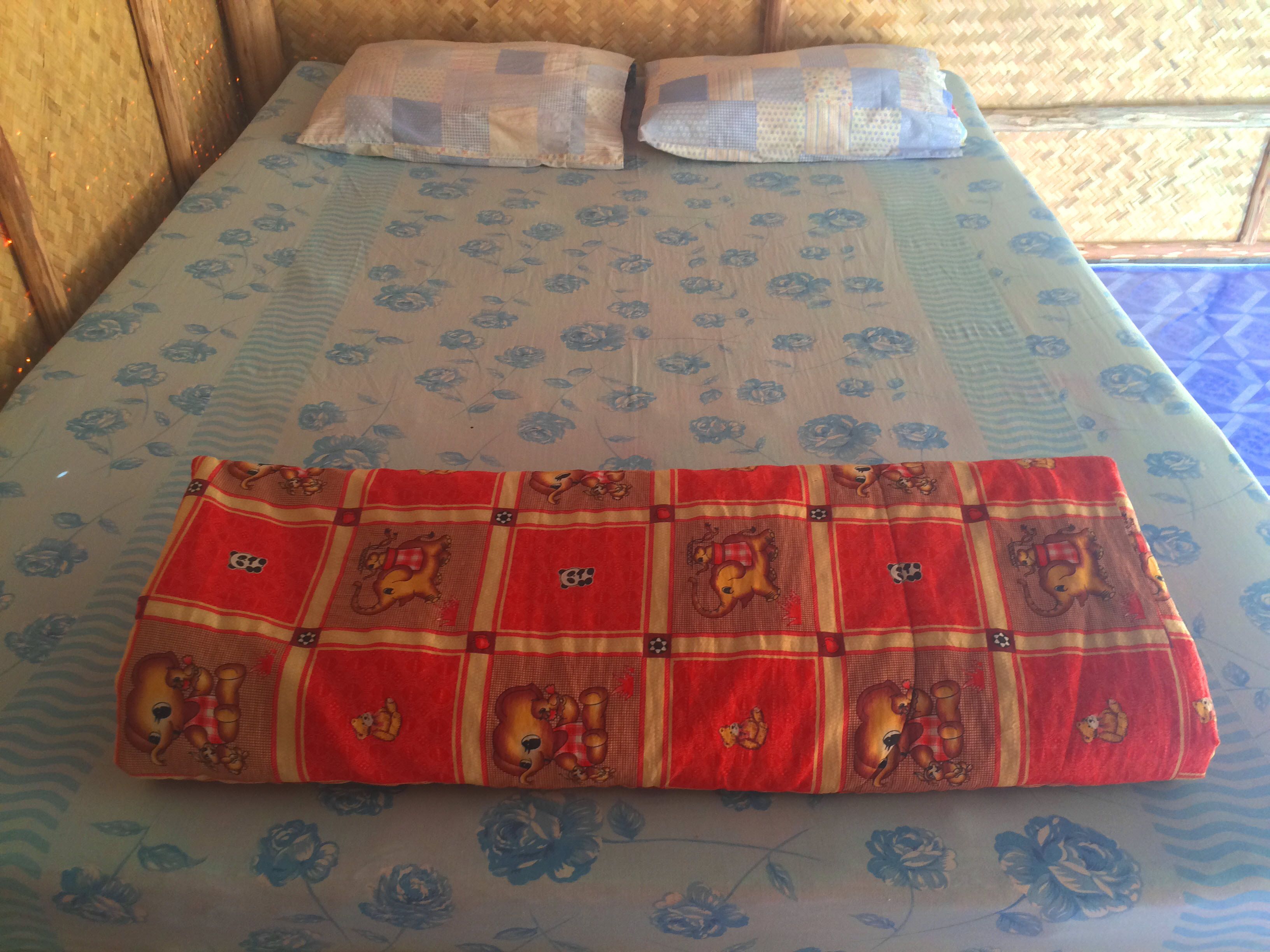 A bed with a floral-patterned bedspread and a red blanket with cartoon characters.