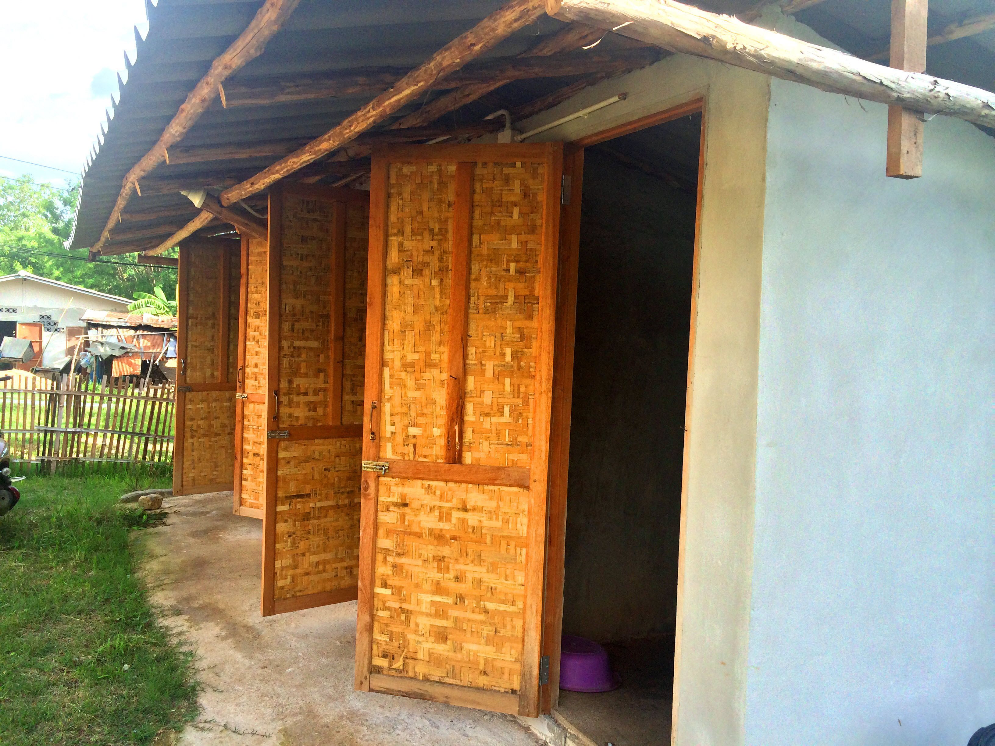 A building with multiple wooden doors and a concrete pathway leading to a fenced area.