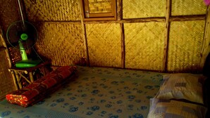 A room with a bed, a green fan, and a woven wall. - Sleepy Hut Pai (Pai)