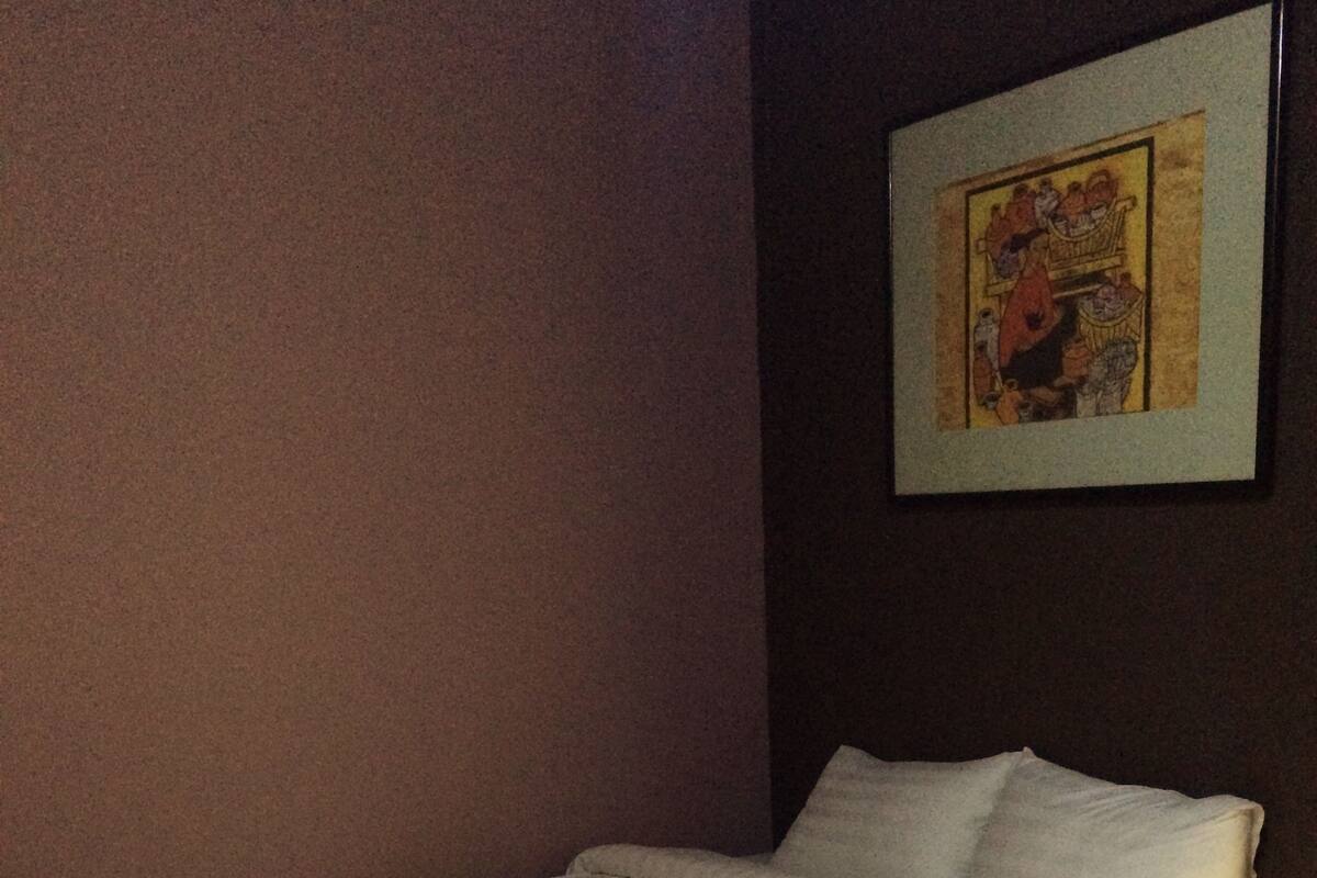 Ein ordentlich bezogenes Bett mit weißen Leinen in einem Zimmer mit Holzboden und dunkler Wand.