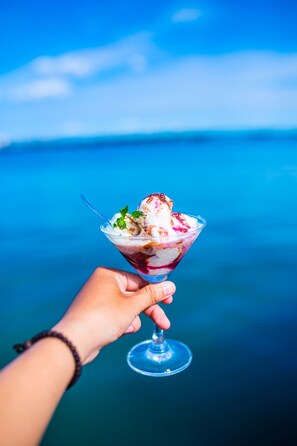 A hand holding a dessert in a glass with a clear view of the ocean in the background. - Geminai Hotel & Cafe (Dong Hoi)