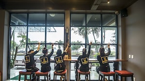 A group of people seated at a bar with large windows overlooking a street. - Geminai Hotel & Cafe (Dong Hoi)