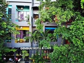 A multi-story hotel with outdoor seating and lush greenery. - Geminai Hotel & Cafe (Dong Hoi)