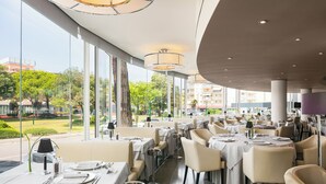Un restaurante con mesas dispuestas para comer, amplias ventanas que ofrecen vistas al exterior e iluminación moderna.