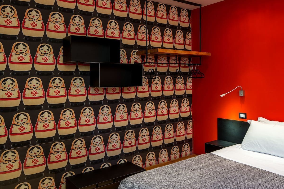 Hotelkamer met een rode wand, een bed met wit beddengoed, een rode plaid, een flatscreen televisie aan de muur en een nachtkastje met een lamp.
