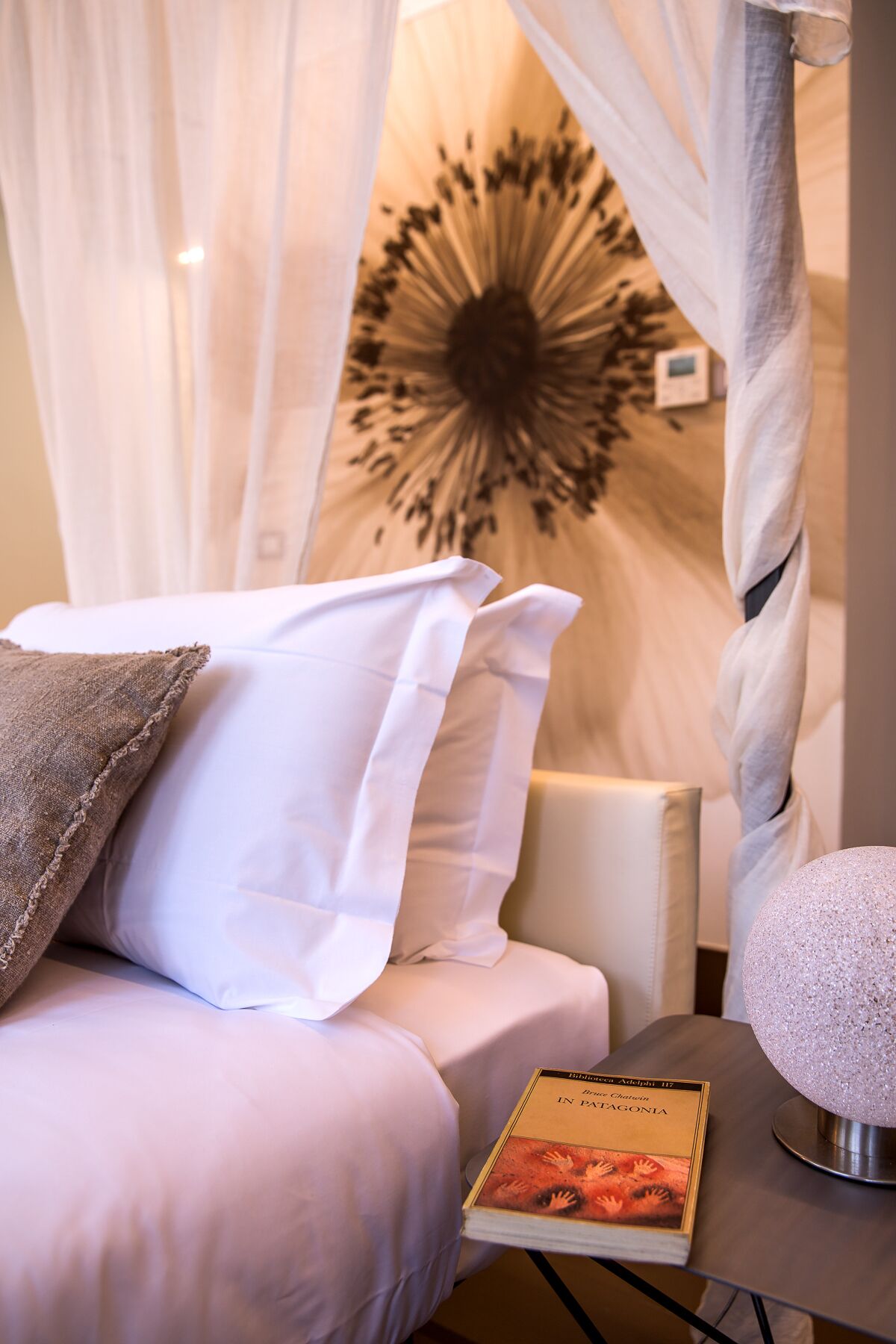 A hotel room with a bed, a bedside table with a book, and a decorative wall piece.