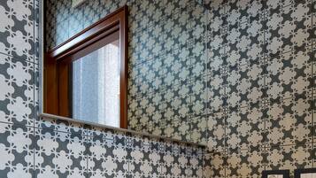 A bathroom with a large mirror, a white sink, and patterned wallpaper.