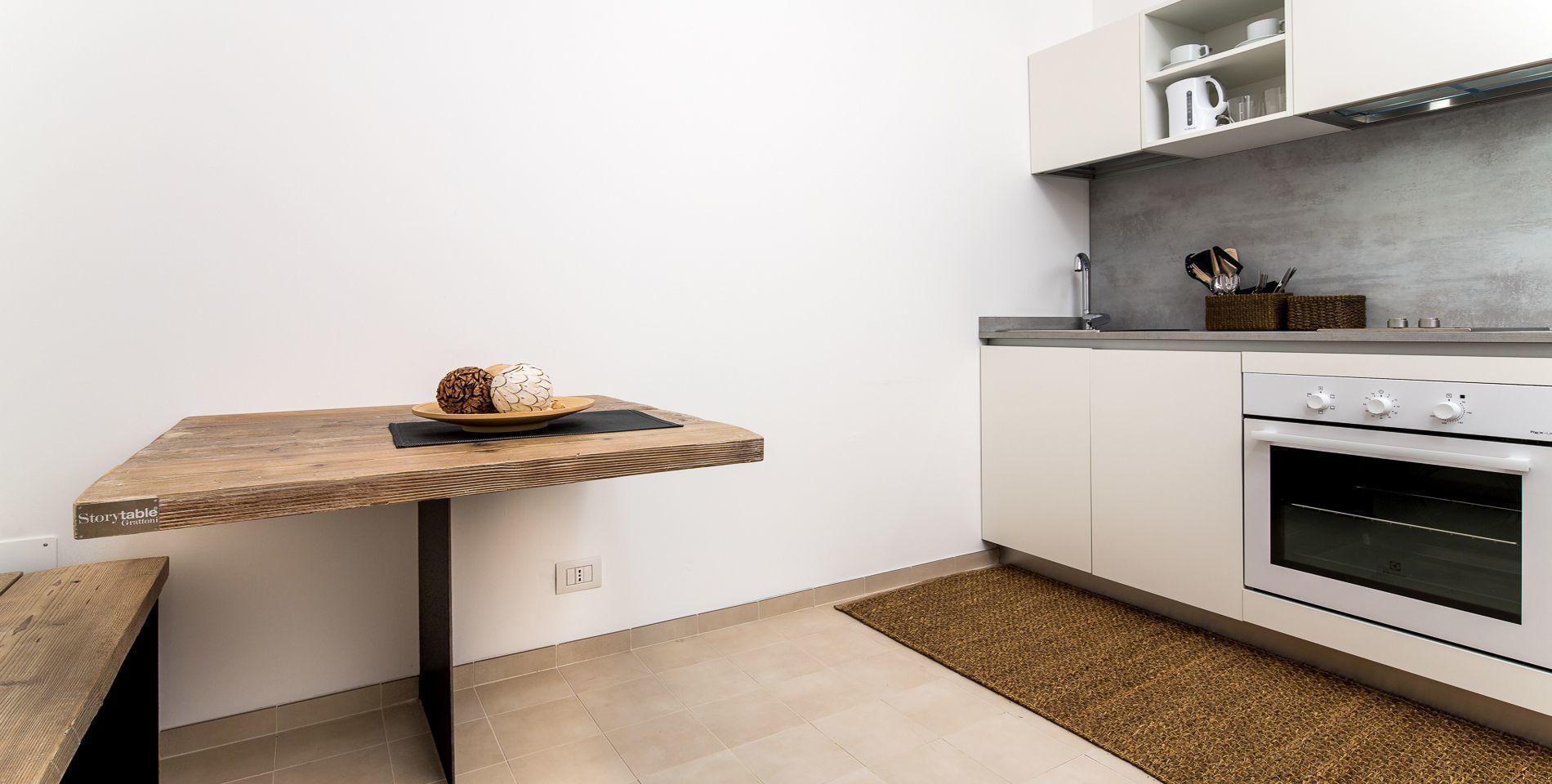 A kitchen with a wooden table, a built-in oven, and a countertop with kitchenware.