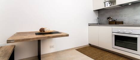 A kitchen with a wooden table, a built-in oven, and a countertop with kitchenware.