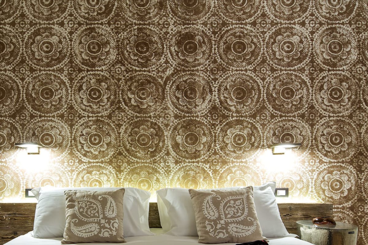 Een hotelkamer met behang met een patroon, een bed met witte lakens en twee wandlampen.