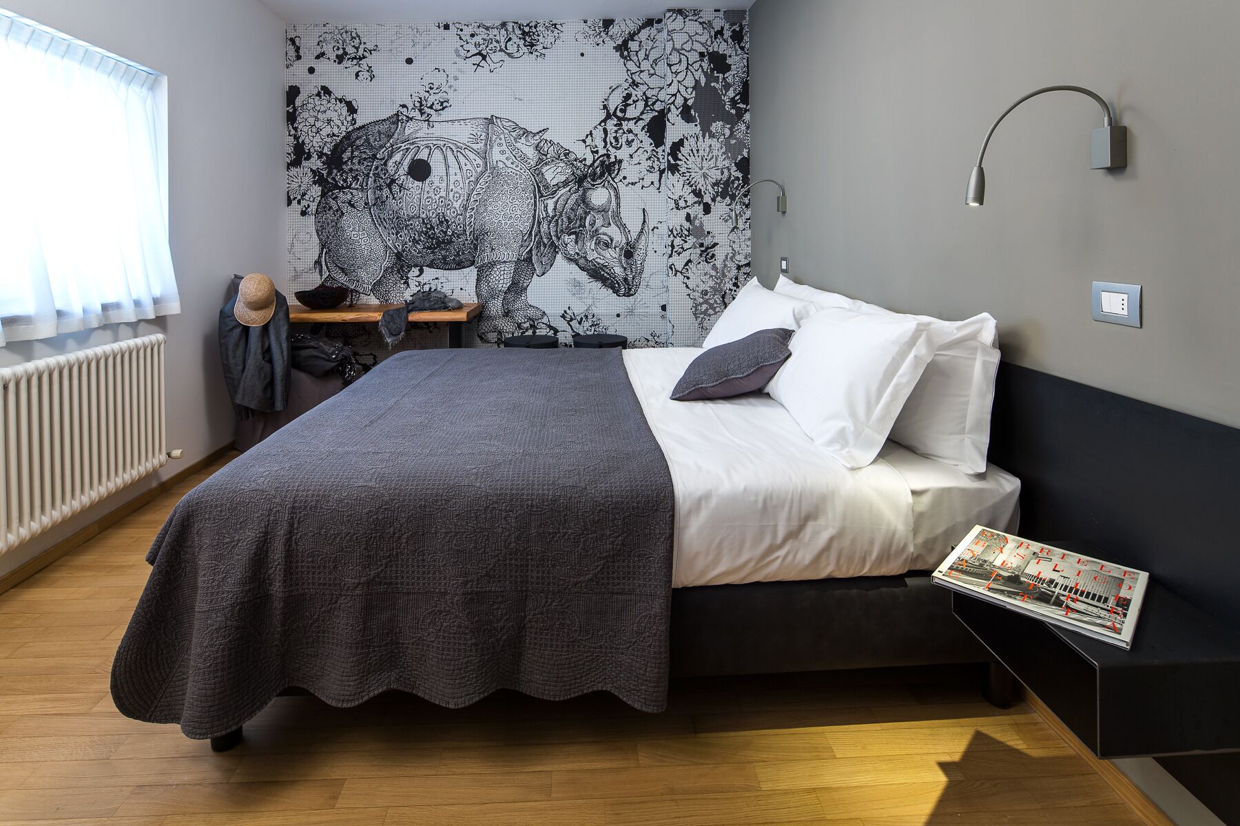 A bedroom with a bed, a nightstand, a lamp, a radiator, and a window with curtains.