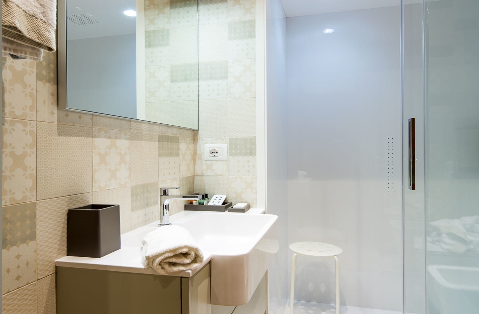 A modern bathroom with a large mirror, a white sink, and a glass shower enclosure.