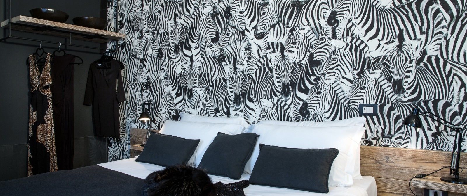 A bedroom with a zebra-patterned wallpaper, a bed with black and white bedding, and a wooden headboard.