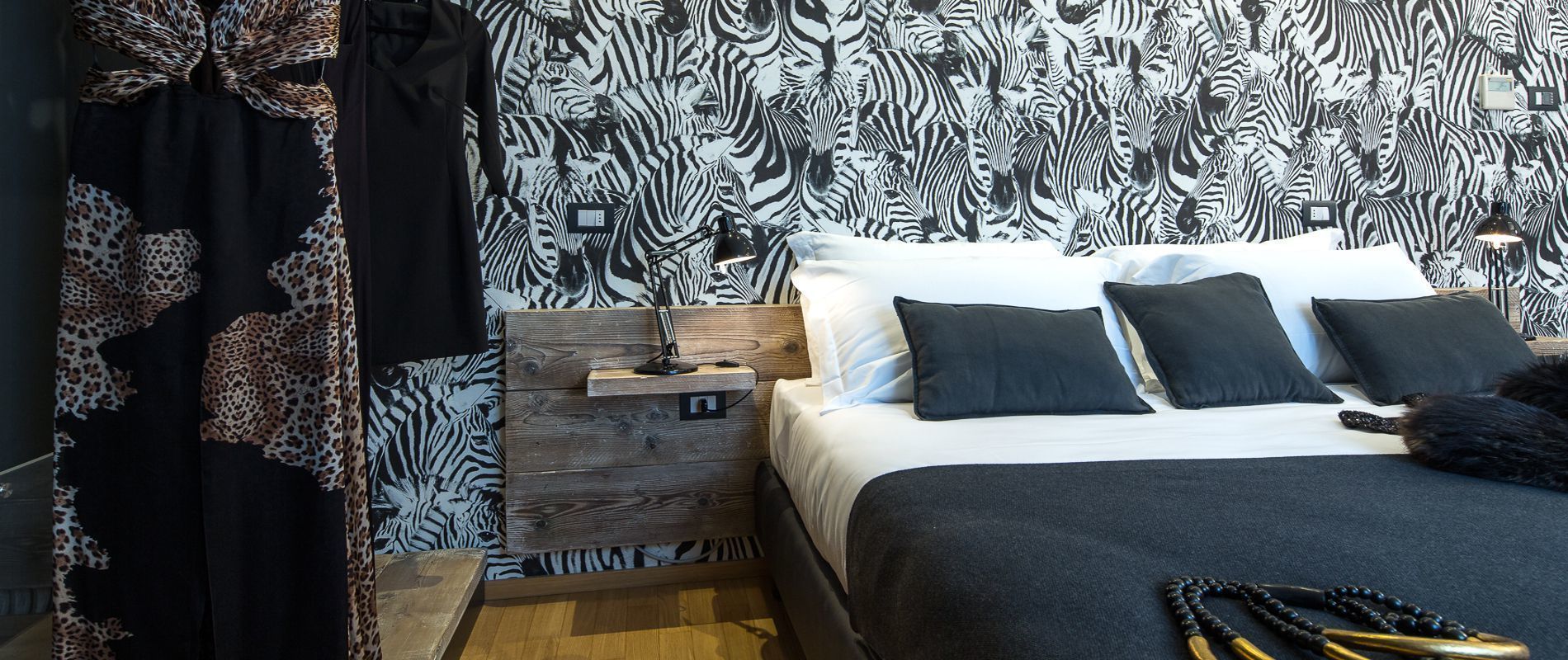 A bedroom with a zebra-striped wallpaper, a wooden nightstand, a bed with black and white bedding, and a black and white patterned curtain.