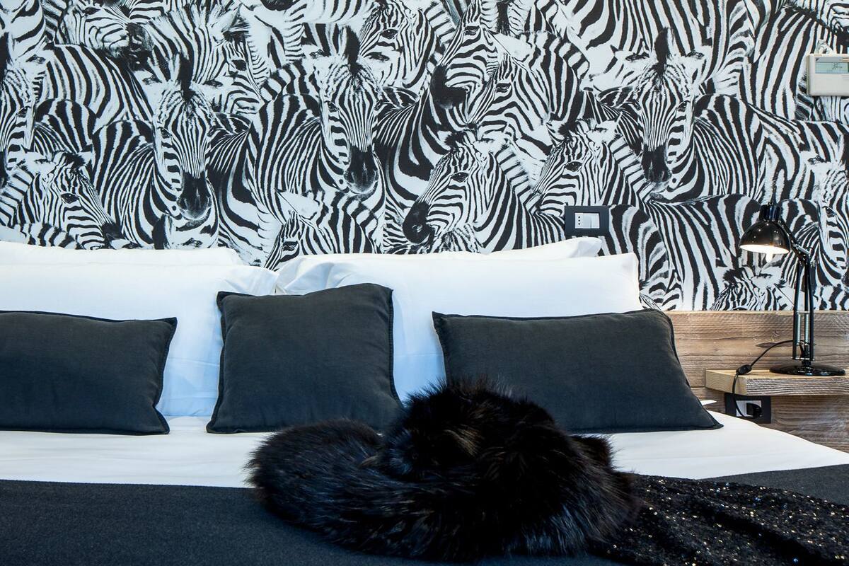 Een slaapkamer met behang met zebraprint, een zwart-wit dekbedovertrek en twee zwarte kussens.