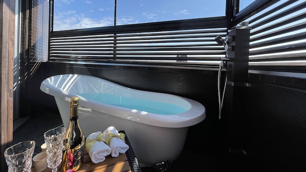 A bathtub with a champagne bottle and towels, a window with blinds, and a view of the sky. - Sendai Hotel Renaissance (Sendai)