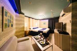 Habitación de hotel con cama, televisión, mesa de comedor con platos y una botella de champán, además de un sofá.