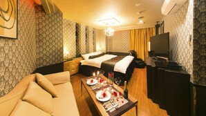 A hotel room with a bed, a sofa, a dining table set for two, a TV, and a minibar. - Sendai Hotel Renaissance (Sendai)