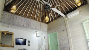 Ein Schlafzimmer mit hoher Decke, Holzbalken, einem Deckenventilator, einem Fernseher, einer grünen Tür und einem Bett mit weißen Leinen.