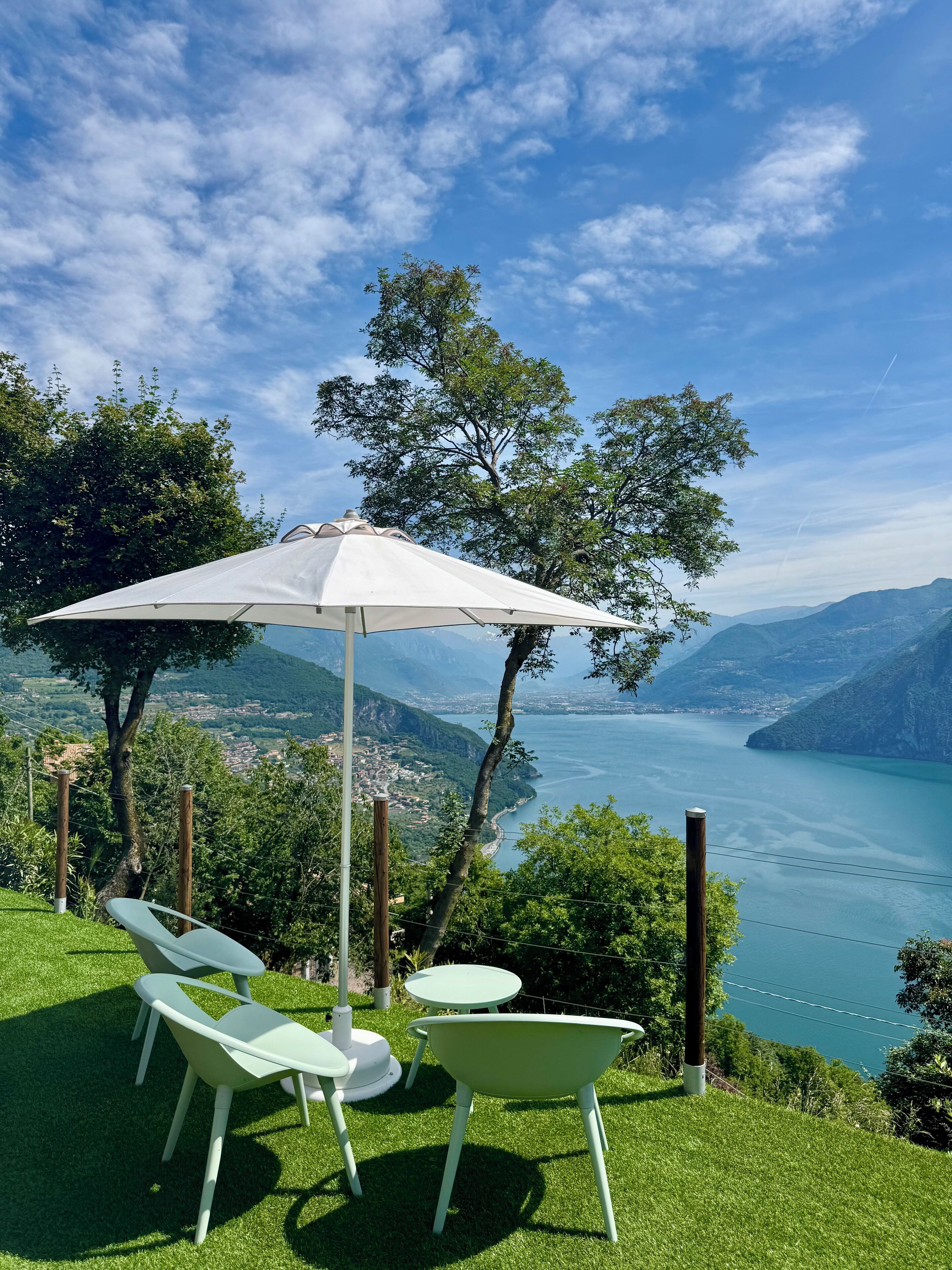 Una terraza con mesa y sillas, una sombrilla y una vista panorámica de un lago y montañas.