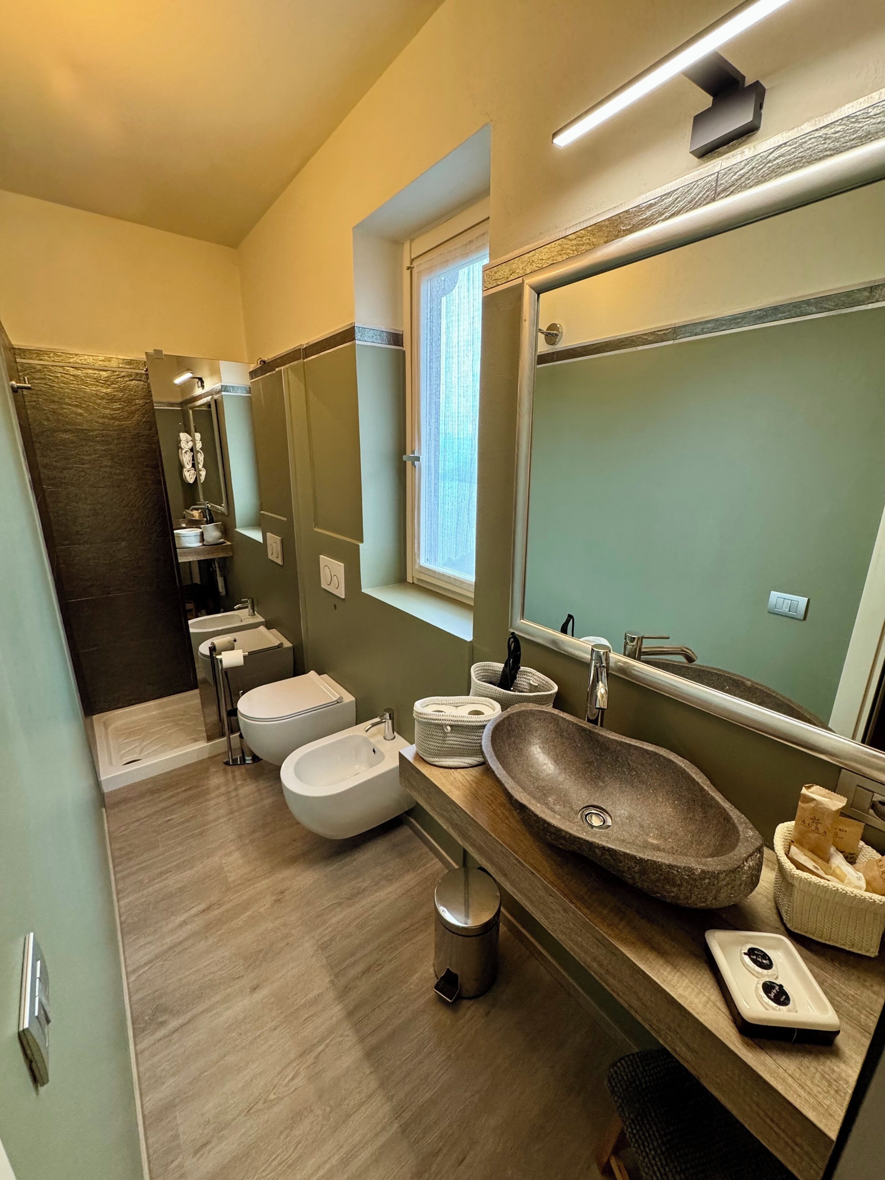 Une salle de bain moderne avec un grand miroir, un lavabo en pierre, un bidet et un espace douche.