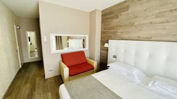 A hotel room with a bed, a red chair, a mirror, and a wooden accent wall.