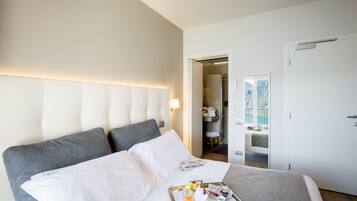 Habitación de hotel con una cama grande, una mesita de noche con una bandeja de desayuno, un baño con ducha y vistas al mar a través de una ventana.